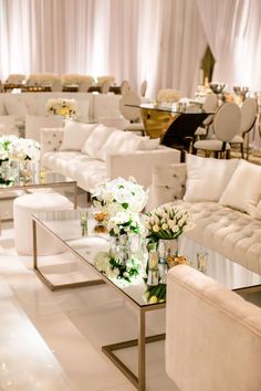 a room filled with lots of white couches and tables covered in flower centerpieces