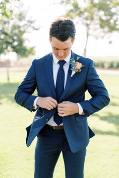 a man in a blue suit and flower boutonniere adjusts his tie