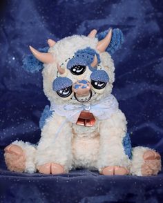 a white stuffed animal with horns and big eyes sitting on a blue cloth covered background