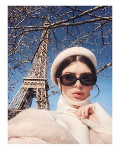 a woman standing in front of the eiffel tower wearing sunglasses and a hat