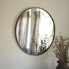 a round mirror hanging on the wall next to a vase filled with dried flowers and plants