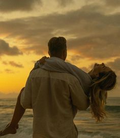 a man carrying a woman on his back as the sun sets over the ocean behind them