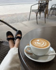 a cup of cappuccino sitting on top of a table next to a woman's legs