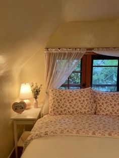 a bed with white sheets and pillows in a bedroom next to a window that looks out onto the woods