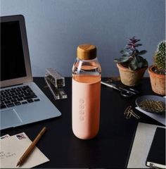 an open laptop computer sitting on top of a desk next to a bottle and pen