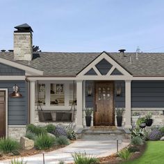 a house that is painted gray and has two brown doors on the front, and some plants