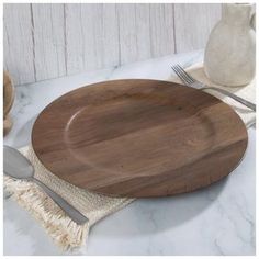 a wooden plate sitting on top of a table next to a white vase and silverware