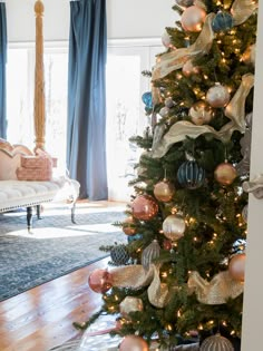 a decorated christmas tree in the corner of a living room with blue drapes and gold ornaments