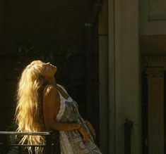 a woman with long blonde hair is sitting on a bench and looking up at the sky