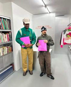 two men standing next to each other holding pink folders