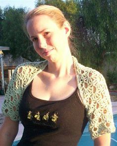 a woman standing in front of a swimming pool wearing a black shirt and green crocheted jacket