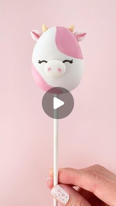 a hand holding a pink and white unicorn lollipop on a toothpick