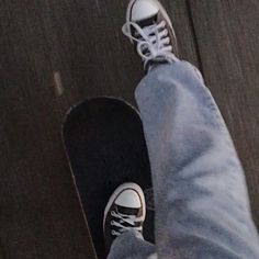 a person wearing white sneakers and jeans standing next to a skateboard