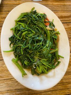 a white plate topped with greens on top of a wooden table