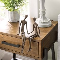 two metal figurines sitting on top of a wooden table next to a vase