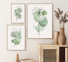 three framed art prints on the wall above a wooden table with vases and flowers