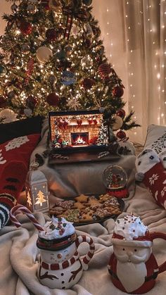 a christmas tree with presents under it next to a laptop and teapots on a blanket