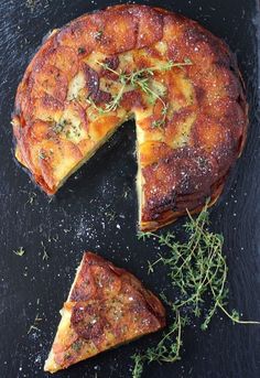 a piece of cheesecake on a black plate with one slice cut out and sprinkled with herbs