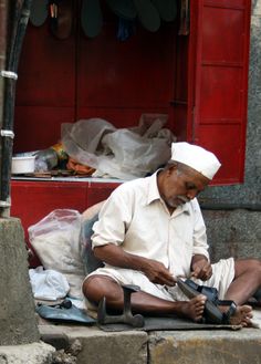 an old man sitting on the ground working with his shoe shiners in front of him