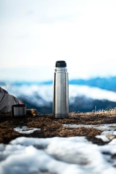 a person laying on top of a snow covered ground next to a bottle and cup