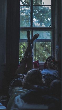 two people laying in bed with their feet up on the window sill and texting