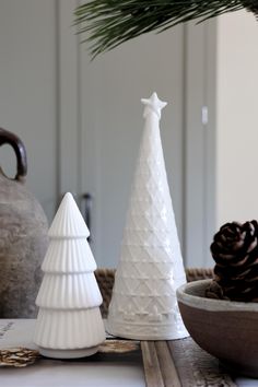 three white ceramic christmas trees sitting on top of a table next to a pine cone