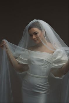 a woman in a white dress with a veil on her head and hands behind her back