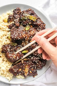 someone is holding chopsticks over rice with meat and vegetables on it, in a white bowl