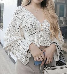 a woman with long hair wearing a white crochet top and holding a purse