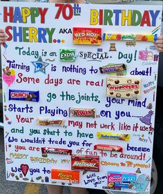 a person holding up a sign with candy on it that says happy 70th birthday