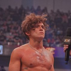 a shirtless man holding a microphone in front of an audience at a wrestling match