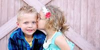 two young children kissing each other in front of a wooden fence