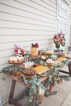 a table with cakes and cupcakes on it in front of a white house