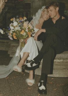 a man and woman sitting on a bench with flowers in their lap, both wearing black shoes