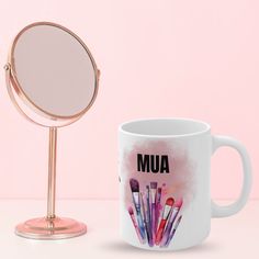 a coffee mug with makeup brushes on it next to a magnifying glass that says mua