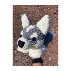 a crocheted gray and white dog is held up by someone's hand