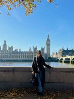 a woman standing on the edge of a wall next to a river with big ben in the background