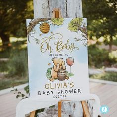 a baby shower sign on an easel with a teddy bear holding a honey pot