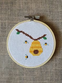 a cross - stitch hoop with a yellow bear hanging from it's side on a tan surface