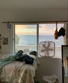 an unmade bed sitting in front of a window next to a wall mounted fan