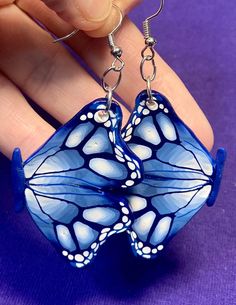 a pair of blue butterfly earrings is being held by a person's hand on a purple background