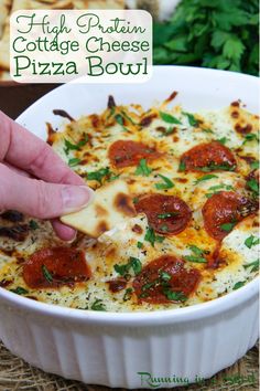 a hand picking up a piece of pizza from a casserole dish with cheese and pepperoni