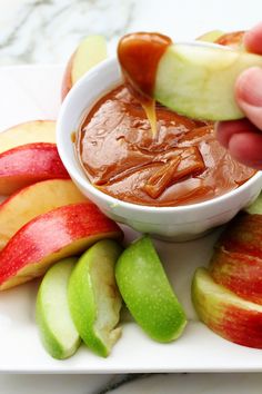 someone dipping apples into a bowl with caramel and apple slices on the side,