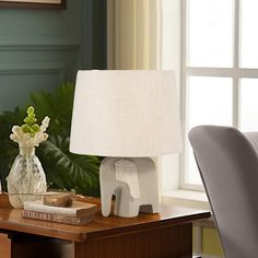 an elephant lamp sitting on top of a wooden table next to a chair and window