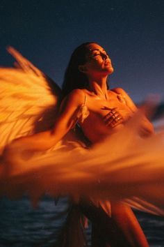 a woman with angel wings in front of a body of water at night or day