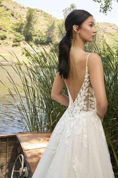 a woman in a wedding dress standing next to a lake and looking back at the camera