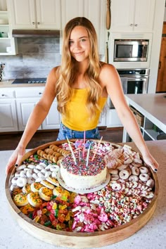 a woman standing in front of a cake with candles on it and lots of sprinkles