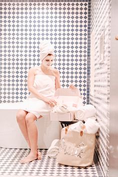 a woman in a white towel is sitting on a bench with a bag and toilet paper