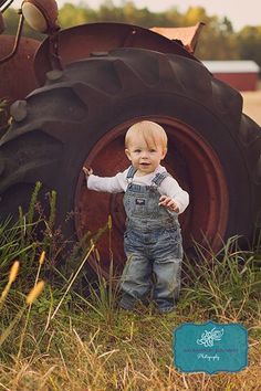 a toddler standing in front of a tractor with his hands on the ground and looking at the camera