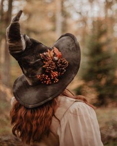 a woman with red hair wearing a brown hat and pointing at the trees in the woods